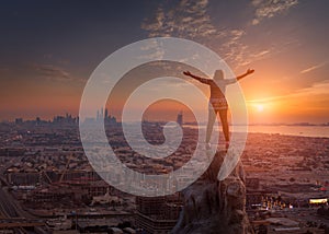 Women standing on the cliff towards the cityscape and setting sun