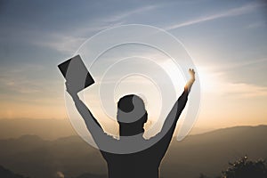 Women standing holding holy  bible for worshipping God at sunset background, Pray to the god, christian silhouette concept