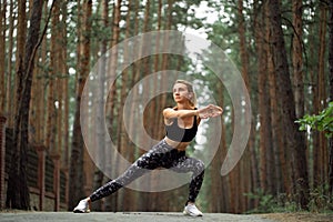 Women stretching arms and breathing fresh air in middle of pinewood forest while exercising. Workouts and Lifestyles