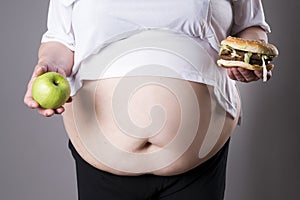 Women suffer from obesity with big hamburger and apple in hands. Junk food concept