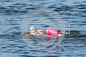 Women swimming alone with pink safety float in blue water