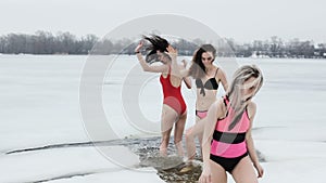 Women in swimsuits frolic in the ice hole.