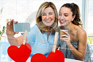 Women taking a selfie on mobile phone against red hanging hearts