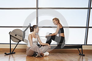 Women Talking At Rowing Machine In Health Club