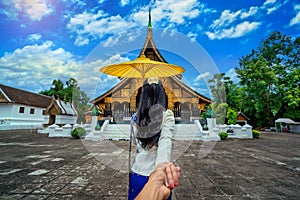 Women tourists holding man`s hand and leading him to Wat Xieng Thong Golden City Temple in Luang Prabang, Laos