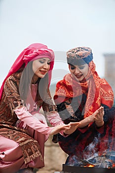 Women in traditional Azerbaijani dress warming hands above the bonfire