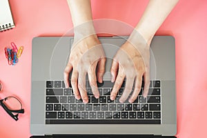 Women typing on laptop in pink pastel colourful office with accessories