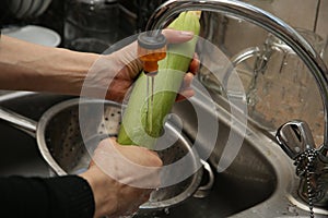 A women using a colander and a kitchen sink to wash an ear of corn.