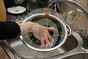 A women using a colander and a kitchen sink to wash marrows.