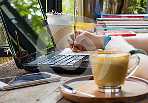 Women are using pencil to write books. Placed on a notebook computer on a wooden desk. Have coffee and a smartphone as a face blur