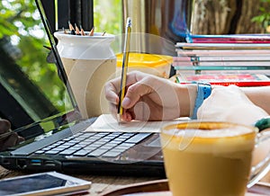 Women are using pencil to write books. Placed on a notebook computer on a wooden desk. Have coffee and a smartphone as a face blur