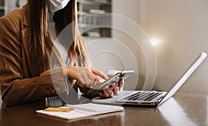 Women are using smartphone and laptop to work at the desk in the morning