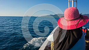 Women in veil and hat on front of boat with blue dark sea and island in distance