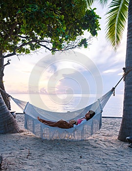 women watching sunrise in a White hammock under palm trees at a tropical beach in Thailand Hua Hin