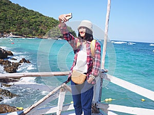 Women wearing Blue jeans and red plaid shirt and backpacking yellow doing Selfie on the bridge at the sea