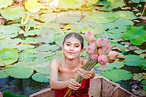 Women wearing traditional Thai clothes sit on a boat carrying large lotus flowers.