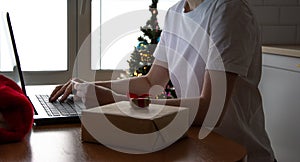 Women wearing white t-shirt using laptop at home office during christmas. Online shopping. Santa`s hat photo