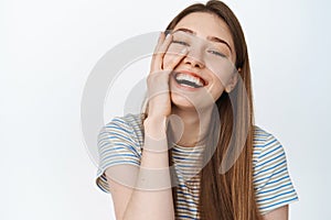 Women wellbeing. Close up of natural beautiful girl, touching clean glowing skin, laughing and smiling, showing white