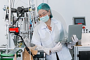 Women worker holding laptop inspector checking quality machine production hygienic mask. face mask manufacturing factory