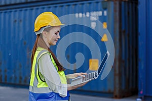 Women worker wear uniform safety helmet using laptop checking containers loading. Area logistics import export and shipping
