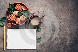 Women workspace with blank notepad, cup of coffee,ceramic bowl with flowers of coral roses and pencil. Top view, flat lay feminine