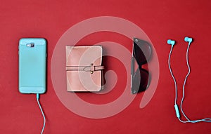 Women& x27;s accessories are lined on a red background. Smartphone, headphones, wallet, sunglasses. Flat lay.