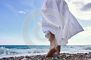 Women& x27;s feet in the sea. Close-up side view of a young woman& x27;s bare feet on a sandy sea beach at sunset.