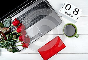 Womens Day background with bouquet of red roses, gift box, calendar with date March 8, cup of coffe and open laptop computer