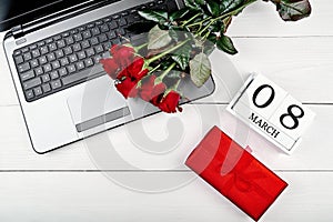 Womens Day background with bouquet of red roses, gift box, calendar with date March 8 and open laptop computer, copy space.
