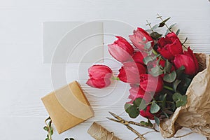 Womens day. Stylish red tulips bouquet, greeting card, gift, scissors, twine on rustic white wood