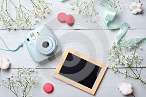 Womens desk with photo camera, picture frame, cookies. Spring minimal flowers frame, pastel colors, flat lay style, top view. Beau