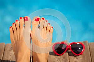 Womens feet with red pedicure against blue water background