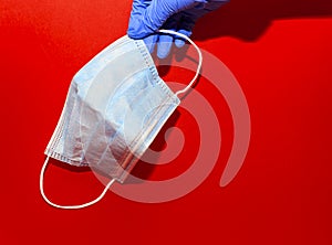 Womens hand in a blue gloves hold a medcine mask on a red background
