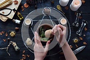 Womens hands make love potion on pentagram circle with candles, stones and old books on witch table. Occult, esoteric or