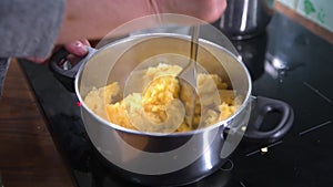 Womens hands mashing patato in pan on kitchen hob, cooking mash potato