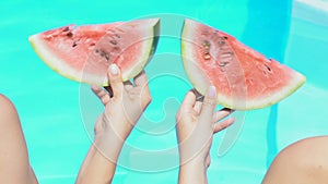 Womens hands simultaneously moving watermelon slices against swimming pool