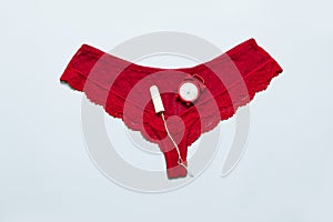 Womens lace red panties with medical female tampon against critical days on a blue background. Menstruation, means of protection