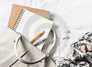 Womens leather handbag, clean blank notepad, pen and scarf on a light background, top view. Free space