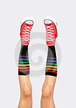 Womens legs in stylish red sneakers and rainbow socks on gray background