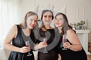Womens party. Girlfriends girls in black dresses kiss the birthday girl. Glasses with pink champagne in hands