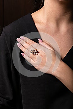 Womens ring of rose gold in the form of a flower with black stones on the finger, on a black background.
