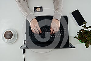 Wonam typing on laptop. Coffee, phone, credit card on the white table.