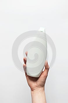 Wonan hand holding shower gel or shampoo plastic container mockup on white background, vertical. Concept beauty treatment
