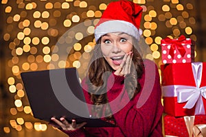 Wondered happy cute girl in santa claus hat using laptop