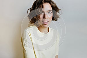 Wonderful brown-haired girl in white shirt spending time at home. Studio portrait of lovable curly female model posing