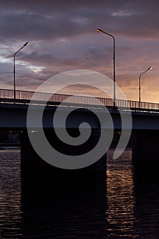 Wonderful evening dusk with sunset sky, clouds, golden sunbeam over black bridge over river with square frame and lantern light.