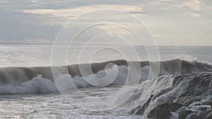 A wonderful evening seascape with a big wave crashing on a dark stone reef. Huge ocean waves break on dark rocks during