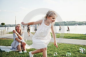 A wonderful girl child makes bubbles with her mom in the park.