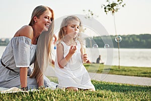 A wonderful girl child makes bubbles with her mom in the park.