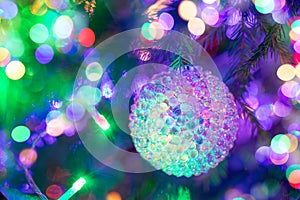 Wonderful glass textured Christmas ball hanging in Xmas tree with multicolored neon holiday lights.